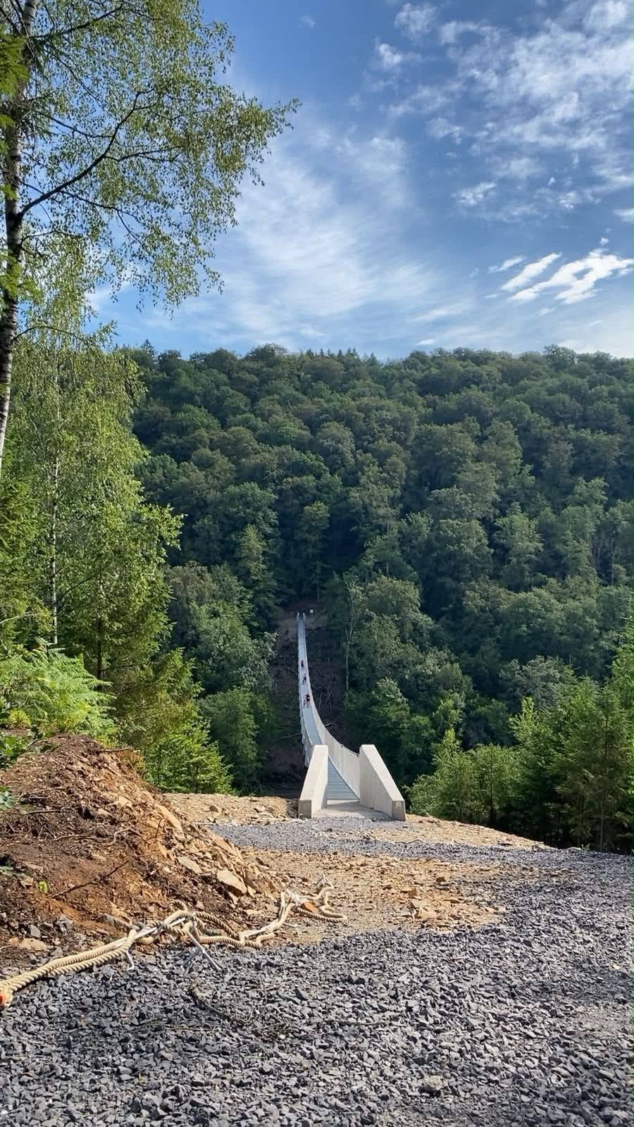 Au bout d’un chemin de gravier, l’entrée de la passerelle entre deux culées de béton, face à la forêt.