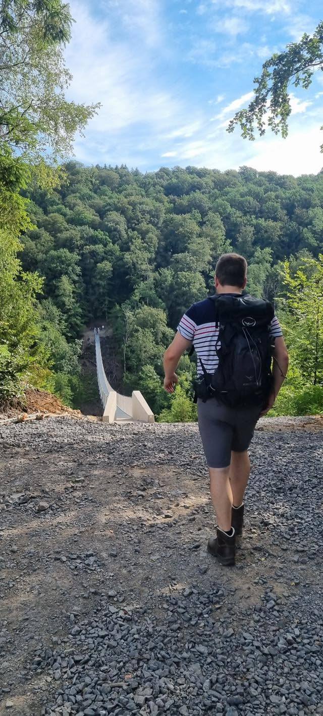Le guide de Guide Rando Trail, sac au dos, marche sur le chemin de gravier vers l’entrée de la passerelle.
