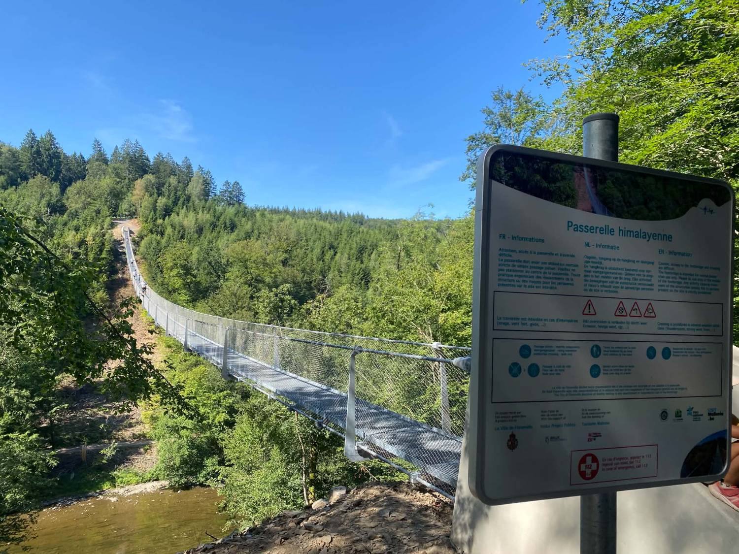Le panneau d’information « Passerelle himalayenne » à l’entrée, en français, néerlandais et anglais, devant la passerelle qui traverse la vallée.